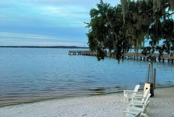 white beach chairs sit on the sandy shore of Lake Minneola in Clermont