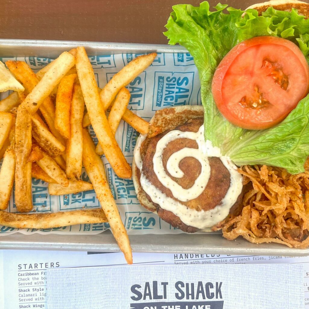 Coastal crab cake sandwich with tomato, lettuce, crispy french fries, and a bed of onion straws
