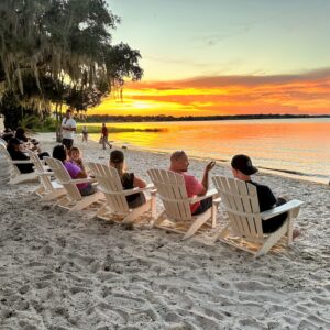 People sit in beach chairs overlooking a sunset over Lake Minneola